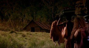 Movie still from “Gorillas in the Mist” (1988), directed by Michael Apted – A person walking in a field near a building; Wide shot, Low angle