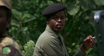 Movie still from “Gorillas in the Mist” (1988), directed by Michael Apted – A man wearing a black hat and a green shirt; Close Up shot, Low angle