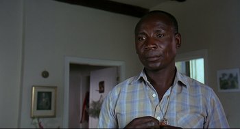 Movie still from “Gorillas in the Mist” (1988), directed by Michael Apted – A man in a plaid shirt is holding a necklace in his hand; Close Up shot, Over the shoulder angle