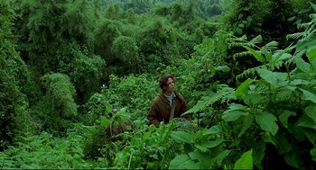 Movie still from “Gorillas in the Mist” (1988), directed by Michael Apted – A man standing in the middle of a lush green forest; Wide shot, Low angle