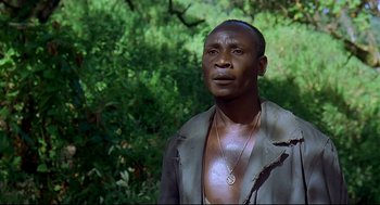 Movie still from “Gorillas in the Mist” (1988), directed by Michael Apted – A man in a jacket standing in front of a tree; Close Up shot, High angle