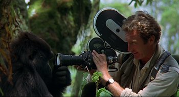 Movie still from “Gorillas in the Mist” (1988), directed by Michael Apted – A man is taking a picture of a gorilla with a video camera; Close Up shot, Low angle