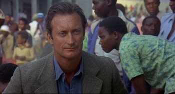 Movie still from “Gorillas in the Mist” (1988), directed by Michael Apted – A person wearing a suit and tie; Close Up shot, Over the shoulder angle