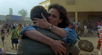 Movie still from “Gorillas in the Mist” (1988), directed by Michael Apted – A man and a woman hugging in front of a crowd; Close Up shot, Over the shoulder angle