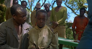 Movie still from “Gorillas in the Mist” (1988), directed by Michael Apted – A group of men standing next to each other in a forest; Medium shot, Over the shoulder angle