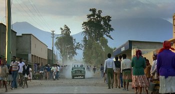 Movie still from “Gorillas in the Mist” (1988), directed by Michael Apted – A group of people standing on a dirt road near a car; Extreme Wide shot, Low angle