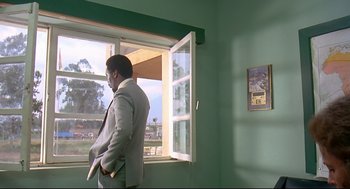 Movie still from “Gorillas in the Mist” (1988), directed by Michael Apted – A man standing in front of an open window; Wide shot, Low angle
