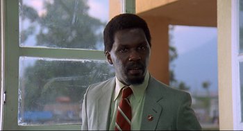 Movie still from “Gorillas in the Mist” (1988), directed by Michael Apted – A man wearing a suit and tie standing in front of a window; Close Up shot, Low angle