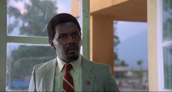 Movie still from “Gorillas in the Mist” (1988), directed by Michael Apted – A man wearing a suit and tie in front of a window; Close Up shot, Low angle