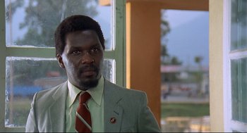 Movie still from “Gorillas in the Mist” (1988), directed by Michael Apted – A man wearing a suit and tie standing in front of a window; Close Up shot, Low angle