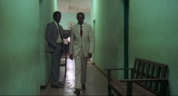 Movie still from “Gorillas in the Mist” (1988), directed by Michael Apted – A couple of men walking down a hall way; Wide shot, Low angle