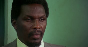 Movie still from “Gorillas in the Mist” (1988), directed by Michael Apted – A person wearing a suit and tie; Close Up shot, Low angle