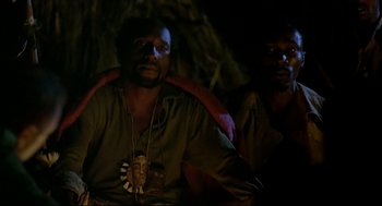 Movie still from “Gorillas in the Mist” (1988), directed by Michael Apted – A man sitting next to another man in a dark room; Close Up shot, High angle