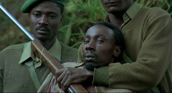 Movie still from “Gorillas in the Mist” (1988), directed by Michael Apted – A group of men standing next to each other holding guns; Close Up shot, Low angle