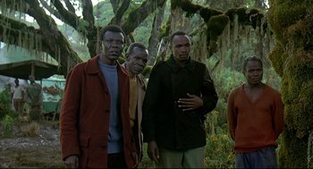 Movie still from “Gorillas in the Mist” (1988), directed by Michael Apted – A group of men standing next to each other in the woods; Medium shot, Low angle