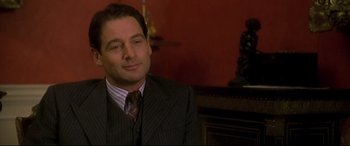 Movie still from “Gosford Park” (2001), directed by Robert Altman – A man wearing a suit and tie sitting in front of a fireplace; Close Up shot, Over the shoulder angle