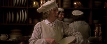 Movie still from “Gosford Park” (2001), directed by Robert Altman – An older woman wearing a chef's hat while holding a pan; Medium shot, Over the shoulder angle