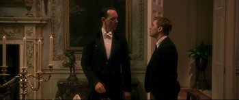 Movie still from “Gosford Park” (2001), directed by Robert Altman – A man in a suit and a man in a bow tie talking to each other in front of a painting; Medium shot, Low angle