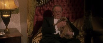 Movie still from “Gosford Park” (2001), directed by Robert Altman – An old man sitting on a couch holding a dog; Medium shot, High angle