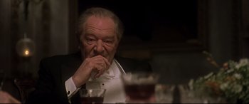Movie still from “Gosford Park” (2001), directed by Robert Altman – An older man sitting at a table with a glass of wine in front of him; Close Up shot, Over the shoulder angle