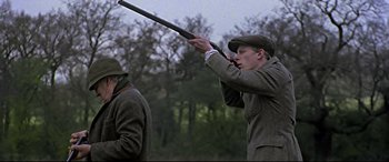 Movie still from “Gosford Park” (2001), directed by Robert Altman – A young man holding a gun while standing next to another man; Medium shot, Low angle
