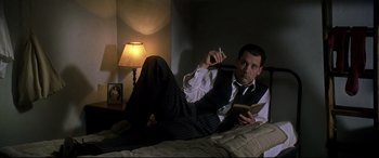 Movie still from “Gosford Park” (2001), directed by Robert Altman – A man laying on a bed reading a book and smoking a cigarette; Medium shot, Low angle