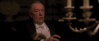 Movie still from “Gosford Park” (2001), directed by Robert Altman – An older man holding a small dog while wearing a tuxedo; Close Up shot, Over the shoulder angle