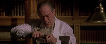 Movie still from “Gosford Park” (2001), directed by Robert Altman – An older man wearing a white lab coat and working on a piece of metal; Close Up shot, Low angle