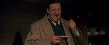 Movie still from “Gosford Park” (2001), directed by Robert Altman – A man in a brown jacket holding a spoon and looking at a cell phone; Close Up shot, High angle