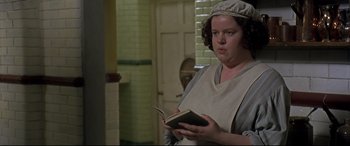 Movie still from “Gosford Park” (2001), directed by Robert Altman – A woman holding an open book while wearing an apron; Close Up shot, High angle