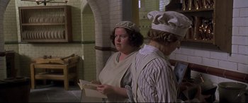 Movie still from “Gosford Park” (2001), directed by Robert Altman – Two people in a kitchen holding papers and wearing hats; Medium shot, High angle