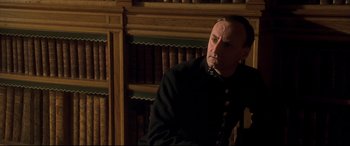 Movie still from “Gosford Park” (2001), directed by Robert Altman – A man wearing a black uniform in front of a book shelf; Close Up shot, Low angle
