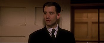 Movie still from “Gosford Park” (2001), directed by Robert Altman – A man wearing a suit and tie standing in front of a door; Close Up shot, Low angle