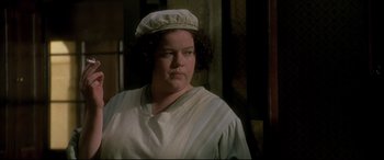 Movie still from “Gosford Park” (2001), directed by Robert Altman – A woman wearing a white hat standing in front of a wall; Close Up shot, High angle