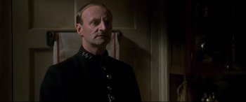 Movie still from “Gosford Park” (2001), directed by Robert Altman – A man in a black uniform standing next to a wall; Close Up shot, Low angle