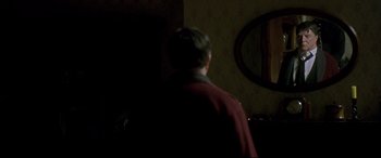 Movie still from “Gosford Park” (2001), directed by Robert Altman – A man standing in front of a mirror in a dark room; Medium shot, Over the shoulder angle