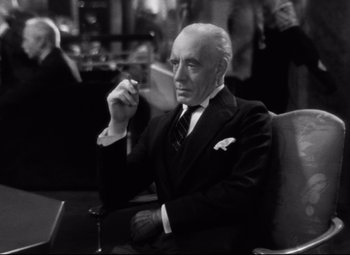 Movie still from “Grand Hotel” (1932), directed by Edmund Goulding – An older man sitting in a chair smoking a cigarette; Medium shot, Low angle