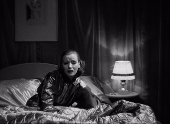 Movie still from “Grand Hotel” (1932), directed by Edmund Goulding – A woman sitting on a bed with a lamp in the background; Medium shot, High angle