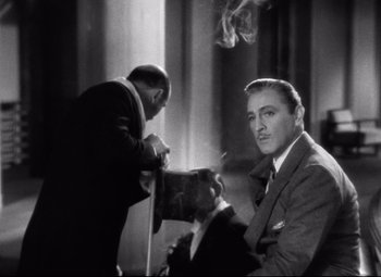Movie still from “Grand Hotel” (1932), directed by Edmund Goulding – A black and white photo of a man smoking a cigarette; Medium shot, Over the shoulder angle