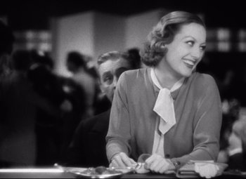 Movie still from “Grand Hotel” (1932), directed by Edmund Goulding – A woman sitting at a table with a man in the background; Medium shot, Over the shoulder angle