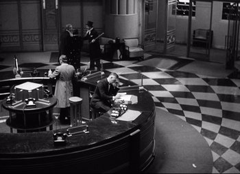 Movie still from “Grand Hotel” (1932), directed by Edmund Goulding – A black and white photo of people sitting at a desk; Wide shot, High angle