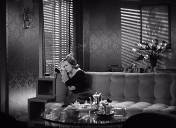 Movie still from “Grand Hotel” (1932), directed by Edmund Goulding – A woman sitting on top of a couch in a living room; Wide shot, High angle