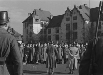 Movie still from “The Grand Illusion” (1937), directed by Jean Renoir – A group of men standing next to each other in front of a building; Wide shot, High angle