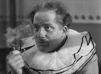 Movie still from “The Grand Illusion” (1937), directed by Jean Renoir – A black and white photo of a man smoking a pipe; Close Up shot, Low angle