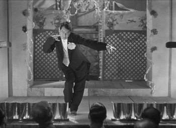 Movie still from “The Grand Illusion” (1937), directed by Jean Renoir – A man standing on a stage in front of a crowd of onlookers; Wide shot, Low angle