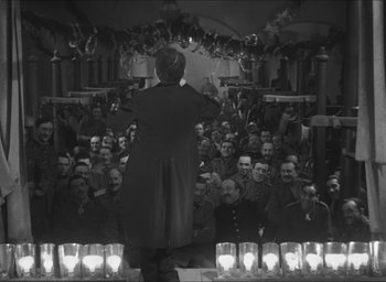 Movie still from “The Grand Illusion” (1937), directed by Jean Renoir – An old photo of a man conducting a crowd of people; Wide shot, High angle