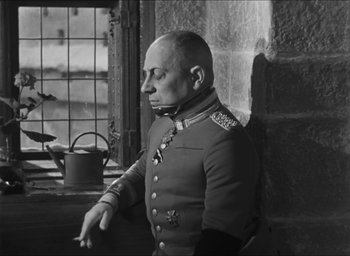 Movie still from “The Grand Illusion” (1937), directed by Jean Renoir – A man in a military uniform is standing in front of a window; Medium shot, Low angle