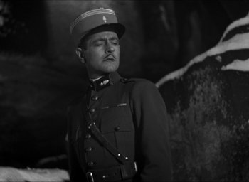Movie still from “The Grand Illusion” (1937), directed by Jean Renoir – A man in a military uniform standing in front of a rock wall; Medium shot, Low angle