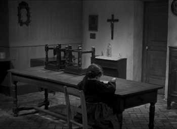 Movie still from “The Grand Illusion” (1937), directed by Jean Renoir – A woman sitting at a wooden table in a room; Wide shot, High angle