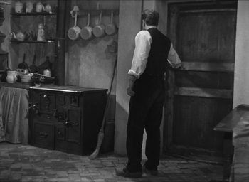 Movie still from “The Grand Illusion” (1937), directed by Jean Renoir – A black and white photo of a man standing in a kitchen; Wide shot, High angle